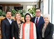 Five professionals pose for a group photo in a bright, modern office lobby, smiling at the camera.