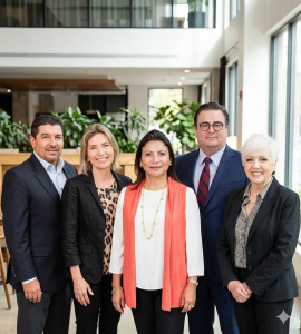 Five professionals pose for a group photo in a bright, modern office lobby, smiling at the camera.