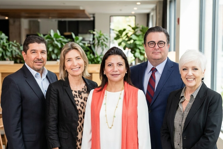Five professionals pose for a group photo in a bright, modern office lobby, smiling at the camera.