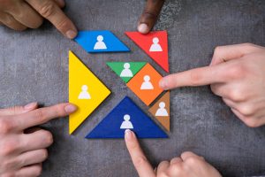 Colorful puzzle pieces with white person icons and several hands pointing to them, illustrating teamwork and collaboration.