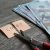 Scissors cutting a sticky note reading 'COST' beside a stack of cash on a wooden table, implying cost cutting.