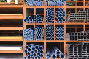 Industrial storage rack with blue PVC pipes organized by size, stacked in orange metal shelving units