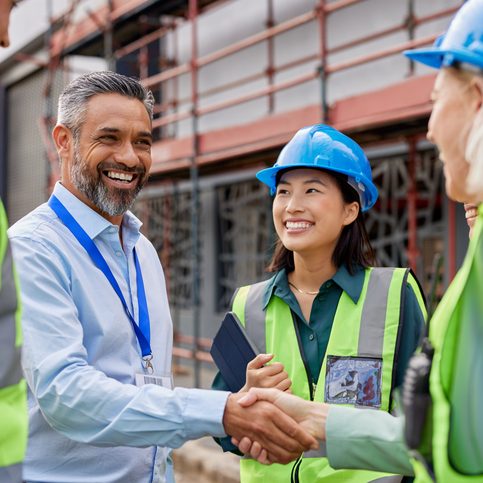 Construction worker shaking hands with foreman Diverse construction team shakes hands on a site with scaffolding behind them.