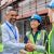 Diverse construction team shakes hands on a site with scaffolding behind them.