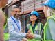 Diverse construction team shakes hands on a site with scaffolding behind them.