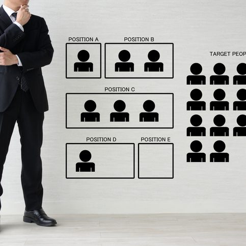Trade Compliance Is No Longer a Back-Office Function Businessman in suit standing beside a wall chart showing recruitment positions A to E and a group of target people icons