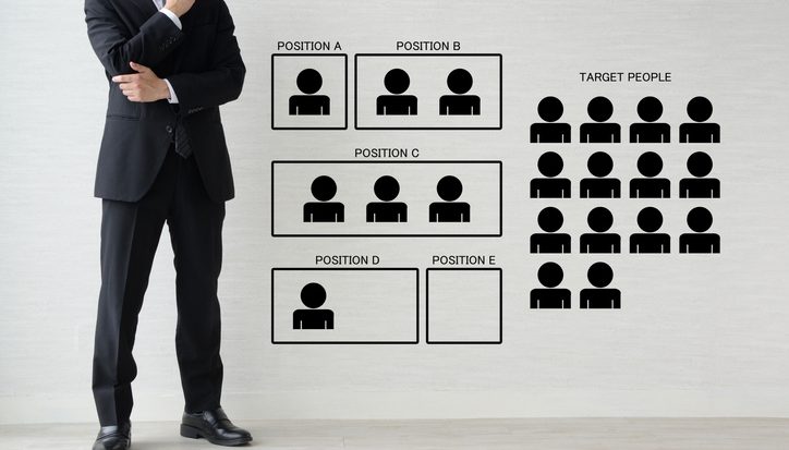 Businessman in suit standing beside a wall chart showing recruitment positions A to E and a group of target people icons